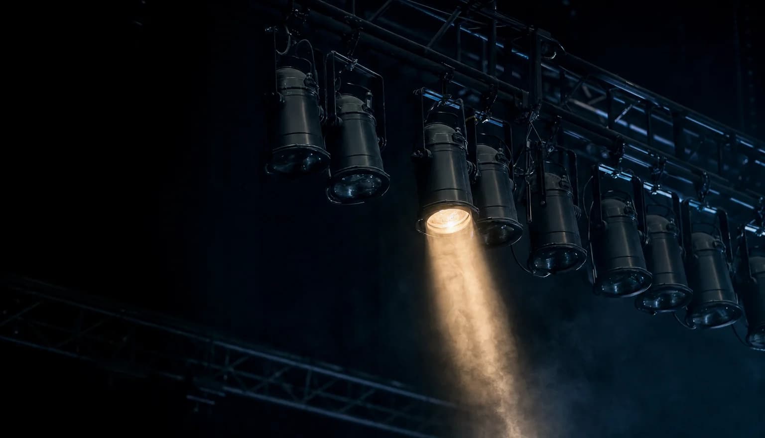 Une grille de projecteurs de scène dans un décor sombre, la plupart éteints et un seul allumé